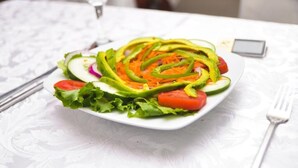 Une assiette de salade composée de laitue, de tomates, de concombres et de tranches d’avocat, le tout servi dans une assiette blanche.