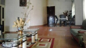 Un salon avec une table basse en verre, un vase contenant des fleurs séchées, un canapé et, au fond, un coin repas.