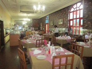 A restaurant with multiple tables set for dining, a bar area, and a view of the outdoors through large windows.