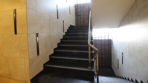 Una escalera con barandilla, flanqueada por paredes con líneas verticales y un ventanal en la parte superior.