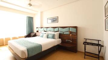 Una habitación de hotel moderna con una cama grande, un cabecero de madera, una mesita de noche y una ventana con cortinas.