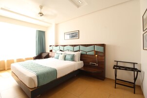 Una habitación de hotel moderna con una cama grande, un cabecero de madera, una mesita de noche y una ventana con cortinas.