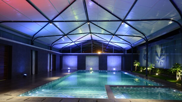 Una piscina interior con techo de vidrio y suelo de baldosas, rodeada de paredes y plantas pequeñas.