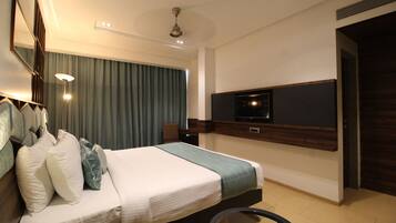A modern hotel room with a large bed, a flat-screen TV mounted on the wall, a ceiling fan, and a large window with curtains.
