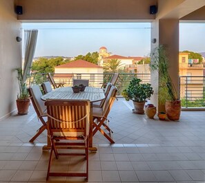 A balcony with a wooden table and chairs, potted plants, and a view of buildings in the background. - Pentari Bitsakis House (Chania)