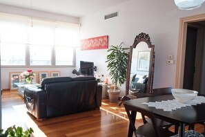 A living room with a black leather sofa, a dining table with a white placemat, a large mirror, and a potted plant. - Pentari Bitsakis House (Chania)