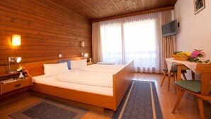 Habitación con paneles de madera, una cama, mesita de noche, lámpara y una pequeña mesa con una silla.