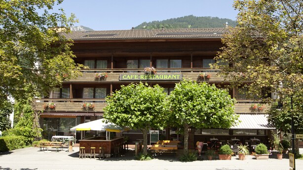 Un café restaurante con terraza al aire libre, rodeado de árboles y plantas en macetas.