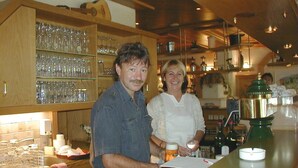 Zona de bar con estantes llenos de vasos y botellas, una barra con caja registradora y una persona sosteniendo un vaso.