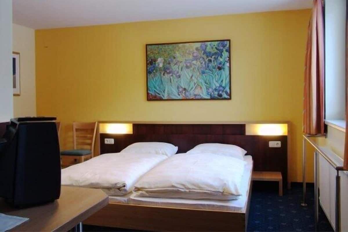 Hotellihuone, jossa on kaksi sänkyä, seinällä taulu ja työpöytä tuolilla.