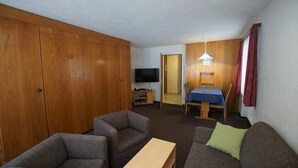 A compact living space with a sofa, a small table, a TV, and a dining area with a table and chairs. - Haus Aida (Saas-Fee)