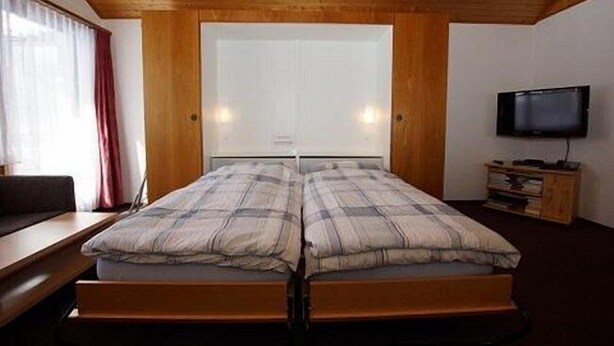 A room with a double bed, a TV, and a wooden ceiling. - Haus Aida (Saas-Fee)