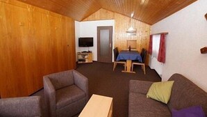 A cozy room with wooden walls and ceiling, a television, a dining table with chairs, and a sofa with cushions. - Haus Aida (Saas-Fee)