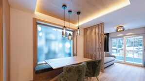 Una zona de menjador moderna amb una taula de fusta, dues cadires tapissades i il·luminació penjant.