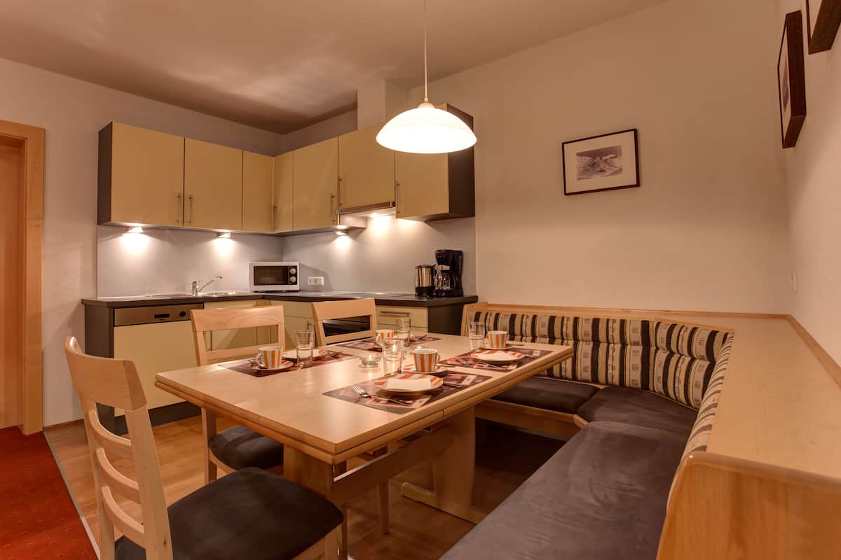 A compact kitchen with wooden cabinets, a dining table with chairs, and a built-in bench with cushions.