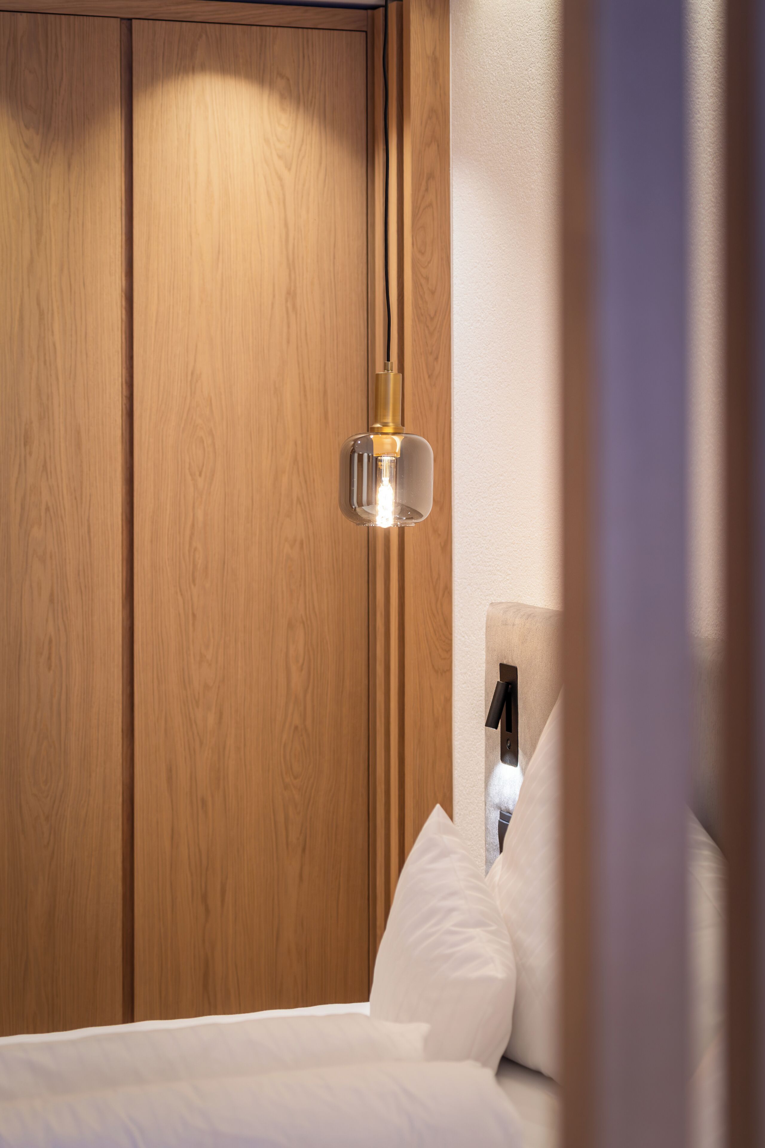 Una camera da letto con pannelli in legno, un letto con biancheria bianca e un lampadario a parete.