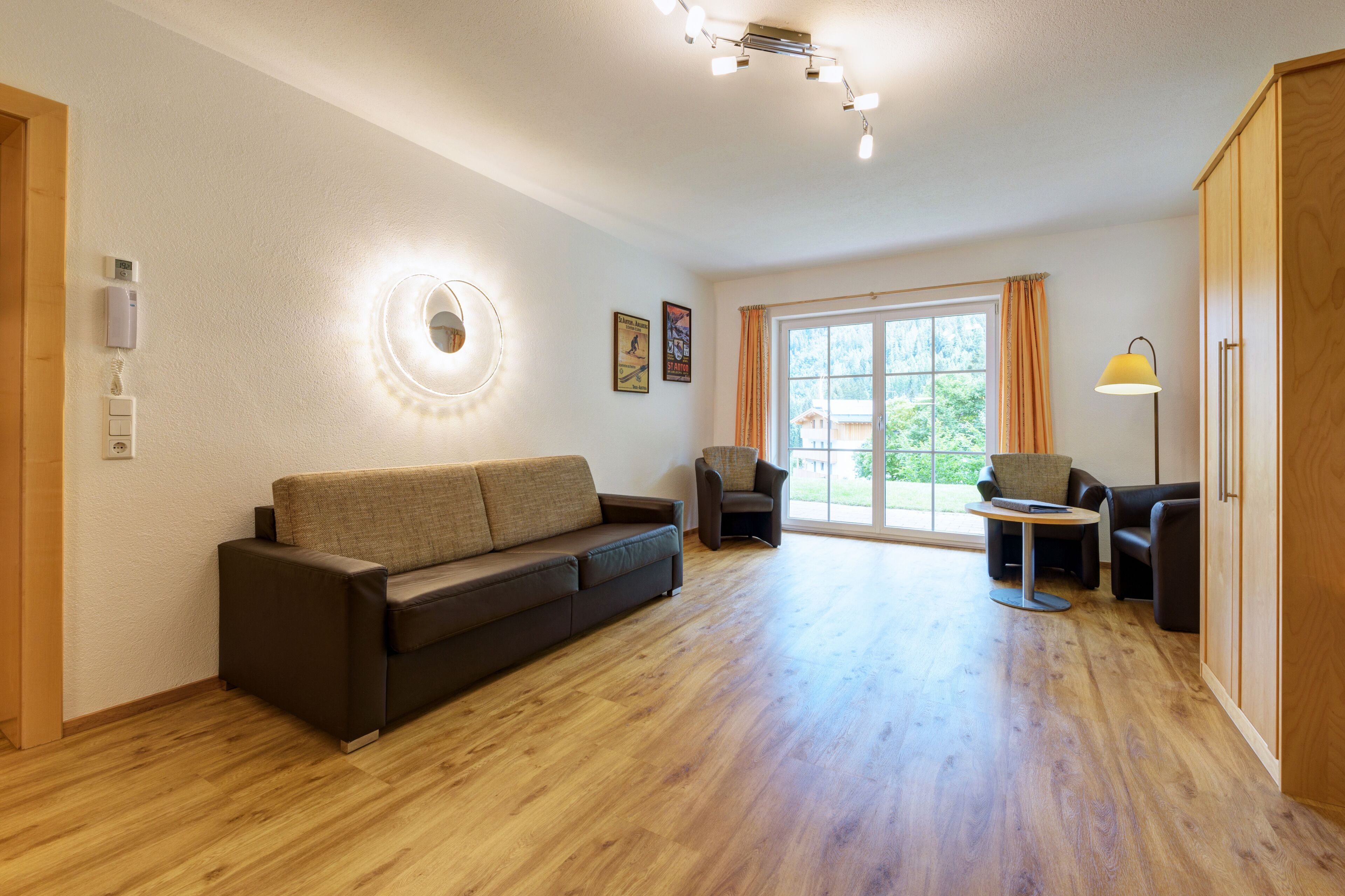 Een ruime woonkamer met houten vloer, een bank, een stoel en een klein tafeltje.