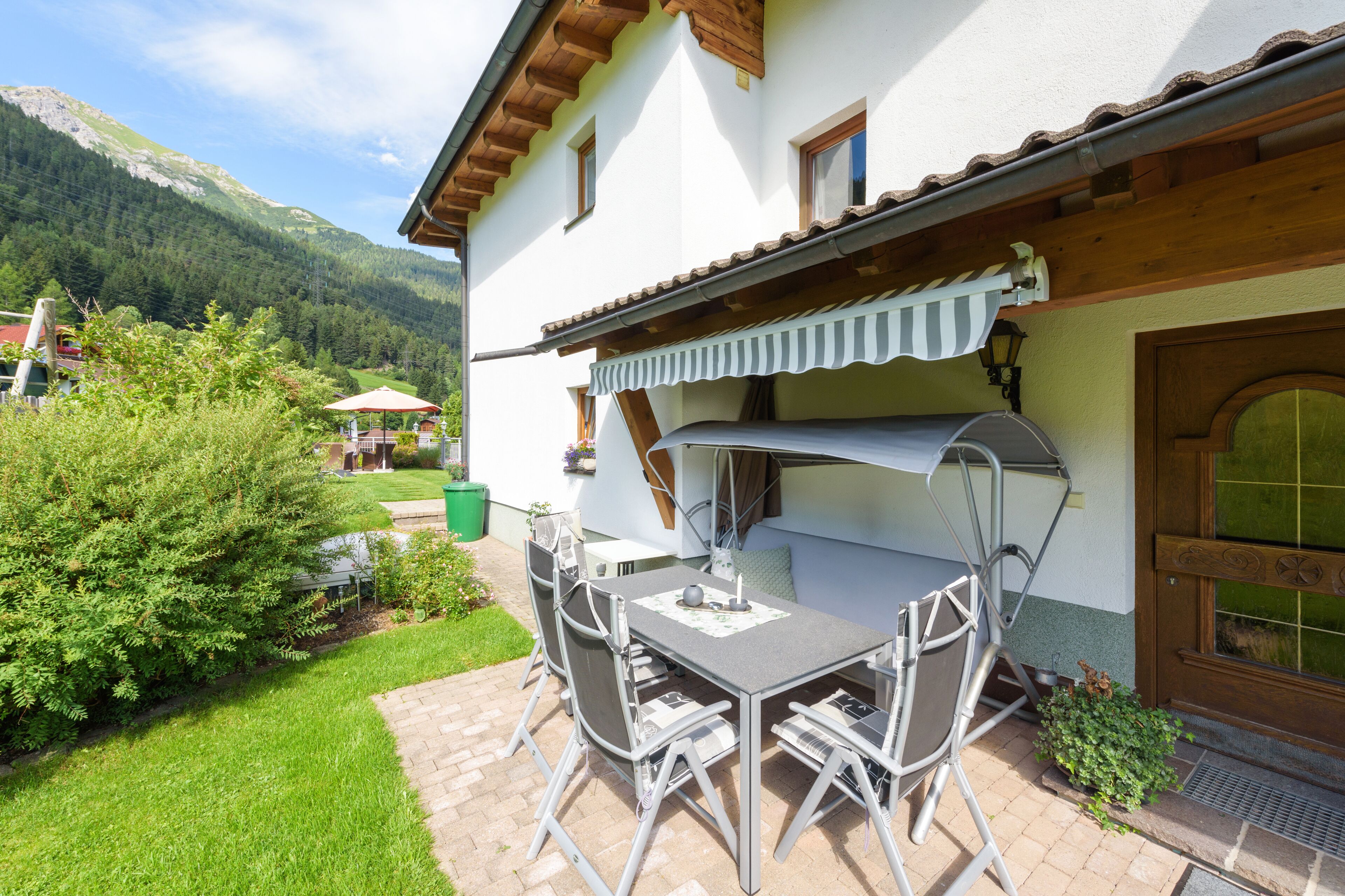 A patio with a table and chairs, a wooden door, and a mountain view.