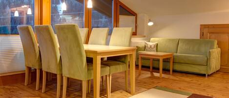 A cozy living room with a wooden dining table, green upholstered chairs, a green sofa, and a small side table.