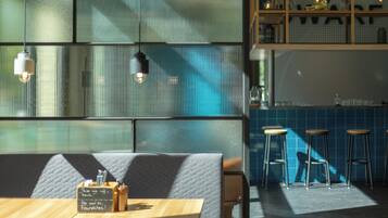 A restaurant interior with a wooden table, cushioned seating, hanging lights, and a blue-tiled backsplash.