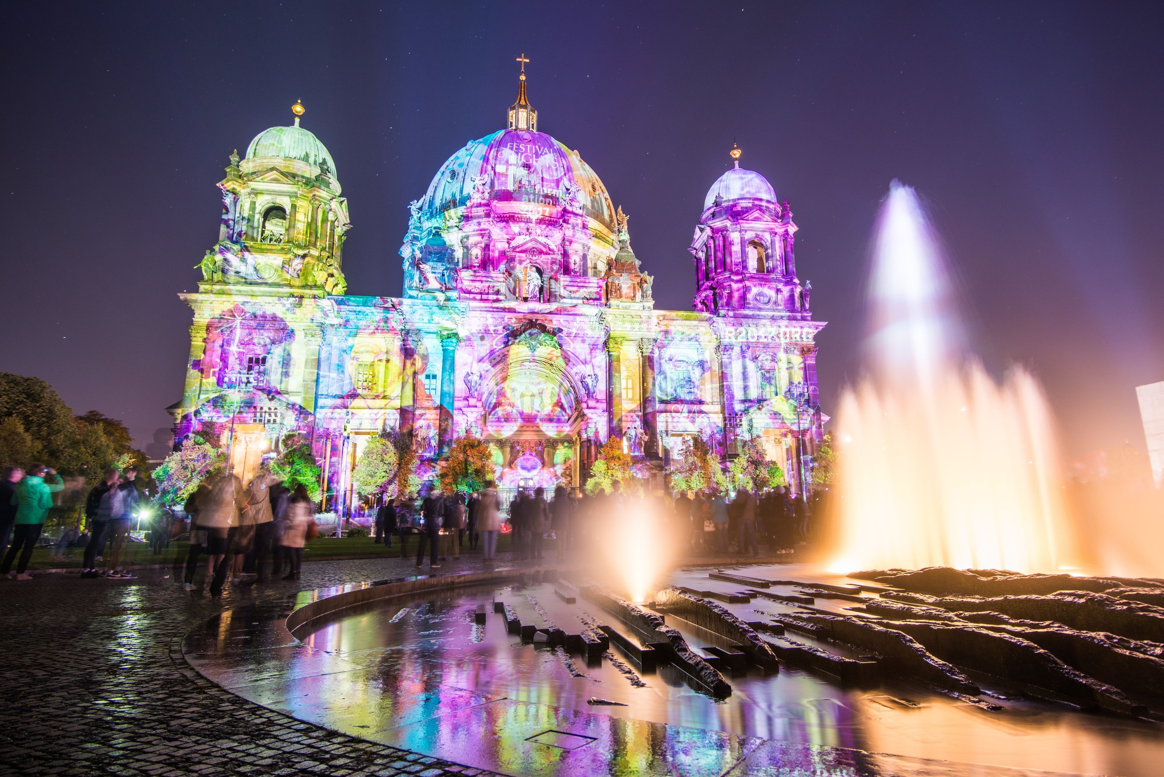A historic building with three domes, a central dome with a cross, and a fountain in front.