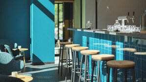 A bar area with stools, a counter, and a blue-tiled wall. - Holiday Inn - the niu, Dwarf Berlin Schöneberg by IHG (Berlin)