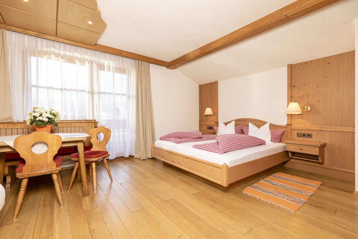 A bedroom with a wooden bed, a desk with a chair, and a window with curtains.