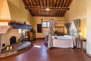 A cozy bedroom with a fireplace, a bed, and a window with curtains. - Villa Fontocchio (Cortona)