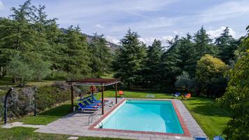 Una piscina rettangolare con una pergola in legno e lettini da relax.