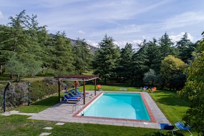 A rectangular swimming pool with a wooden pergola and lounge chairs. - Villa Fontocchio (Cortona)