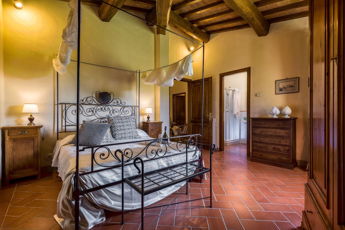 A bedroom with a four-poster bed, wooden headboard, and a tiled floor.