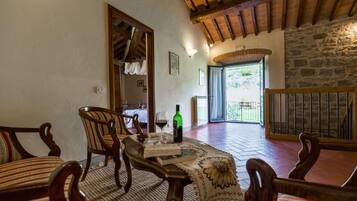A cozy dining area with wooden furniture, a table with a book and a bottle of wine, and a view of the outdoors through a doorway.
