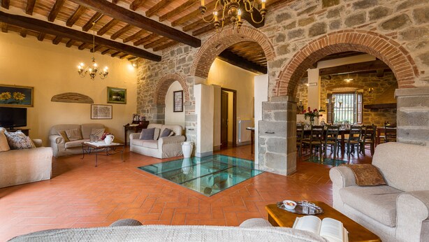 Ein großzügiger Wohnbereich mit Glastisch, Sofas und einem Essbereich mit Steinwand und Holzbalken.