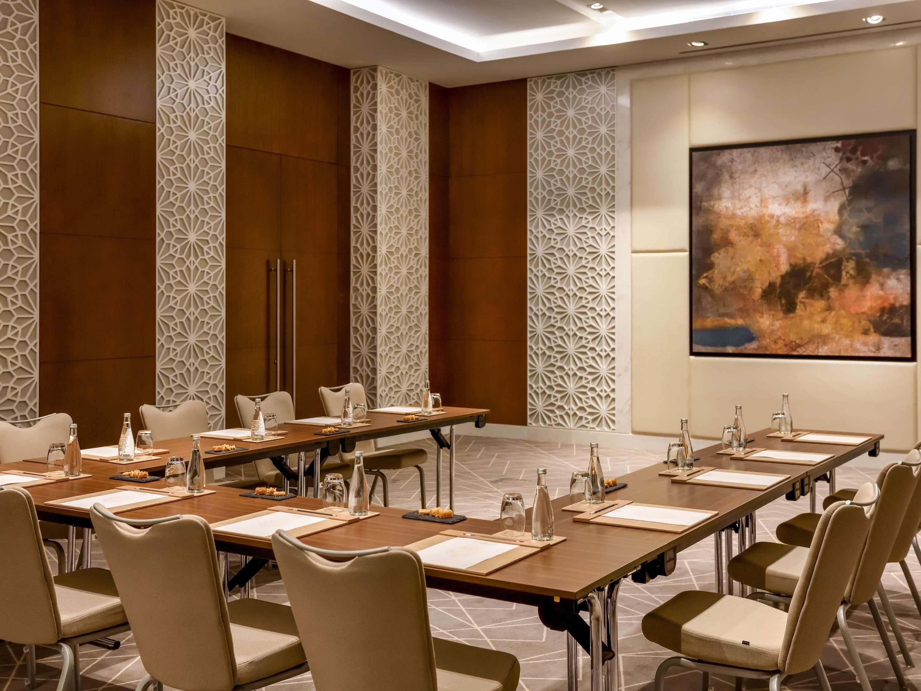 A conference room with a long table, chairs, water bottles, and a projector screen.