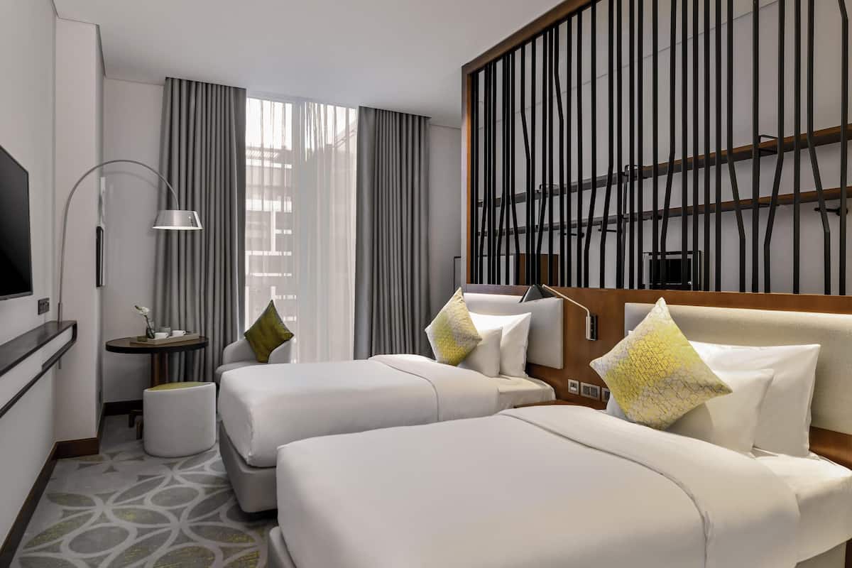 Une chambre d’hôtel avec deux lits, une télévision, un bureau et une grande fenêtre avec des rideaux.