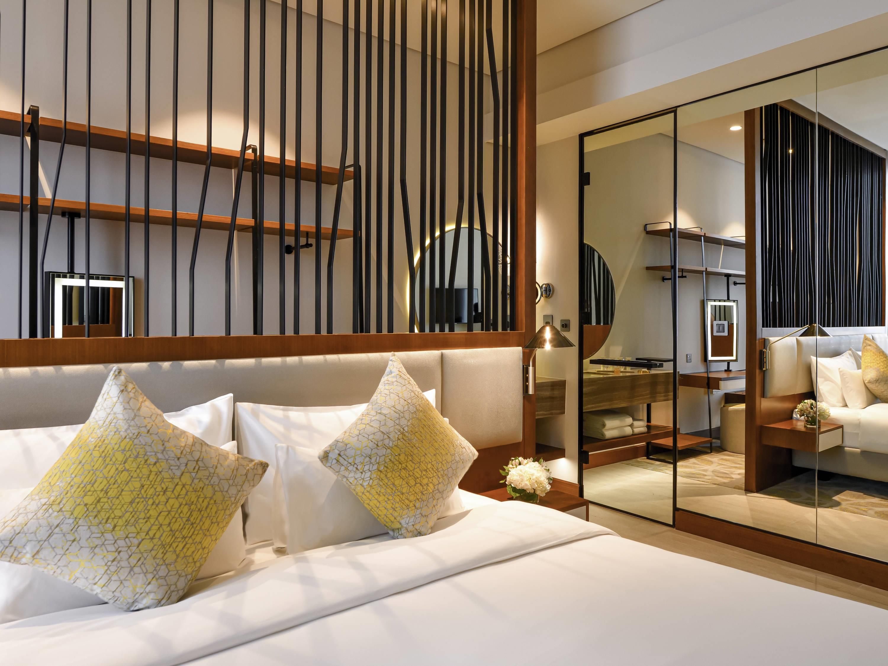 A modern hotel room with a large bed, a wooden headboard, and a glass partition.
