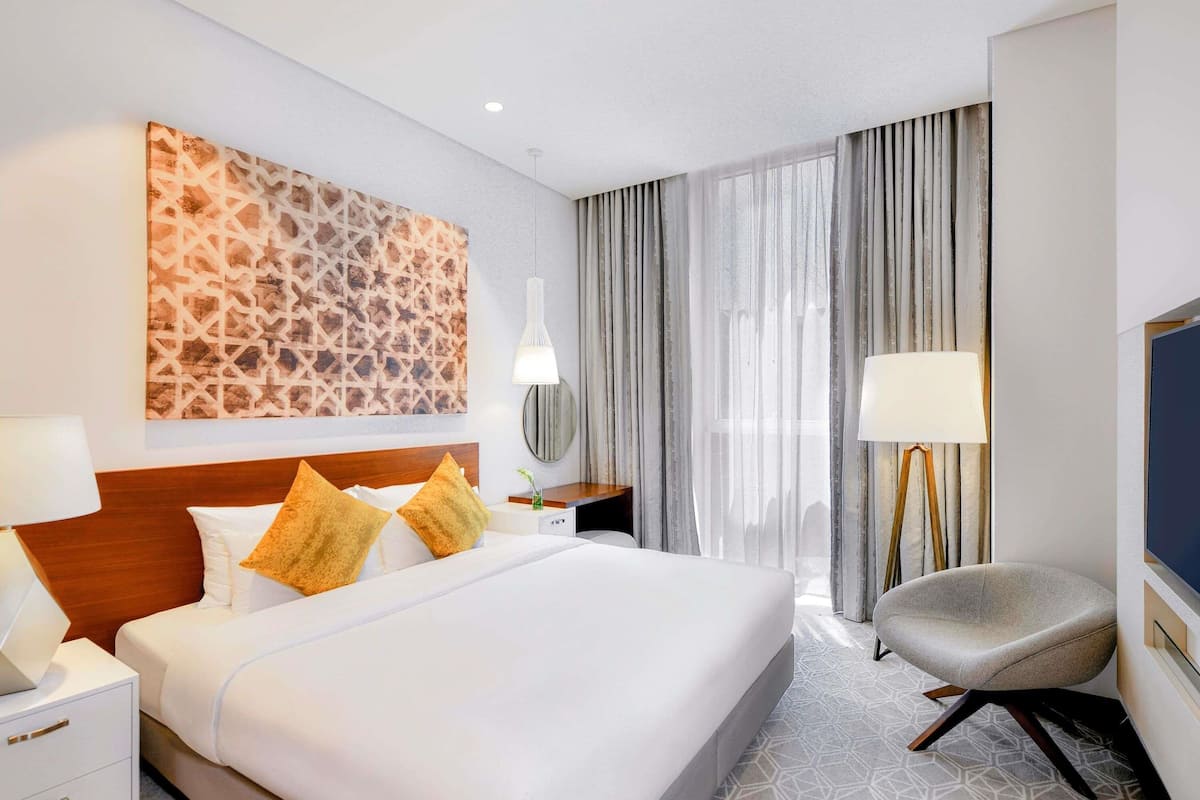Une chambre d’hôtel avec un grand lit, des tables de chevet, une chaise, une télévision et une fenêtre avec des rideaux.