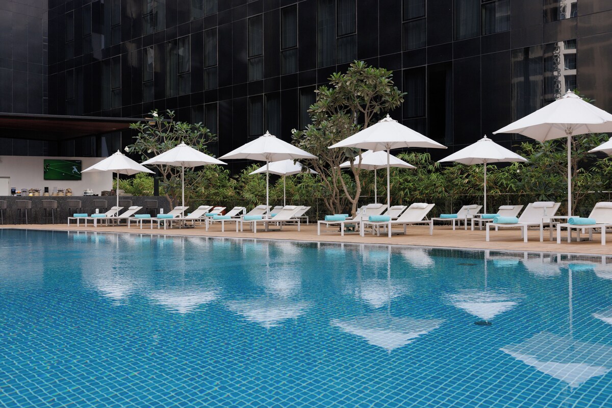 Une piscine entourée de chaises longues et de parasols, le tout adossé à un bâtiment moderne.
