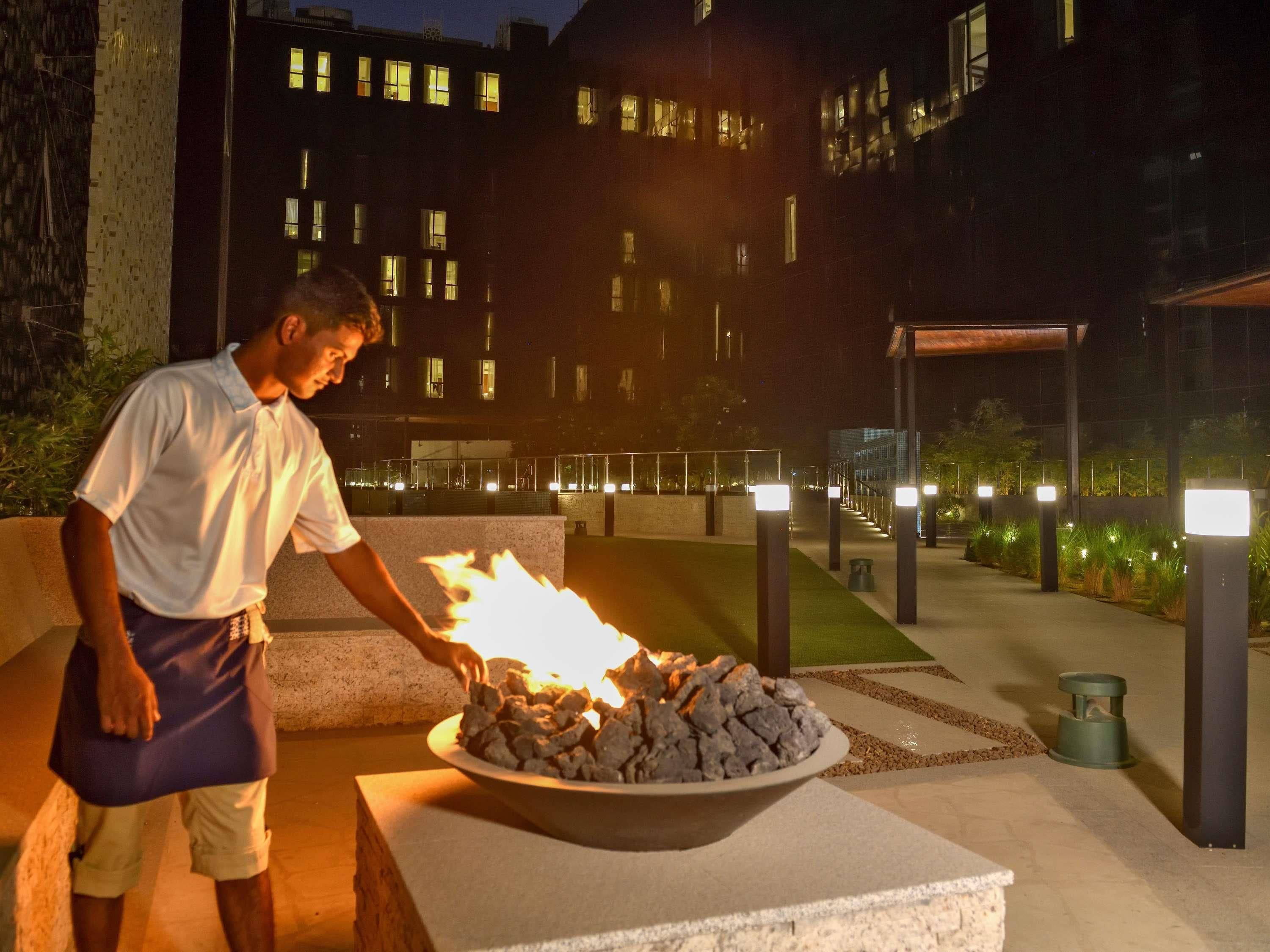Una persona cuidando una chimenea al aire libre, con un edificio de fondo.