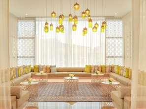 Uma sala de estar ampla, com um sofá grande, várias mesinhas e luminárias pendentes.