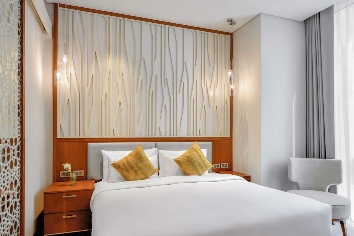 Une chambre d’hôtel avec un grand lit, une tête de lit en bois, une table de chevet, une chaise et un panneau décoratif au mur.
