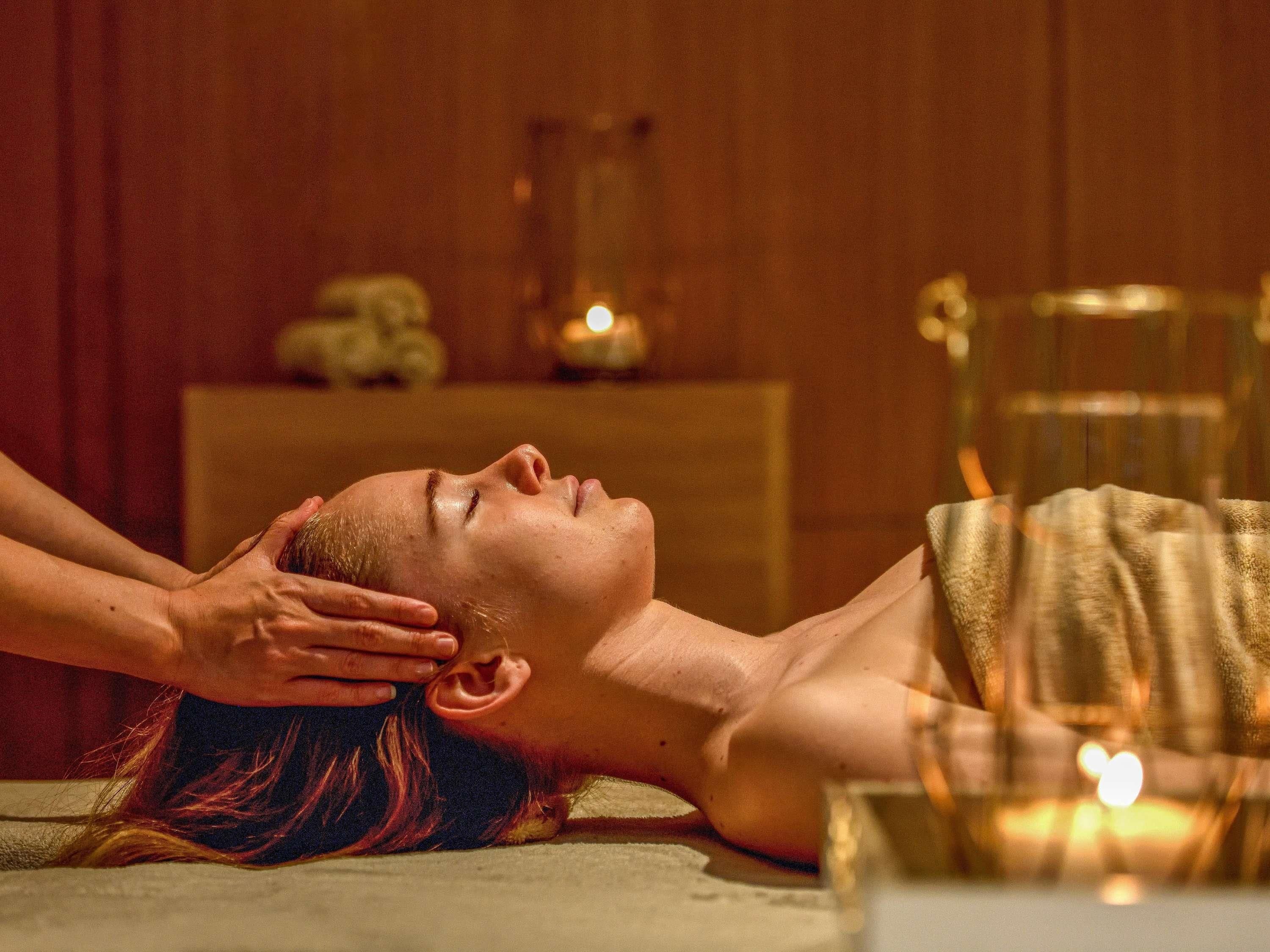 A person receiving a head massage in a room with wooden walls and a small table with candles.