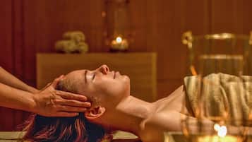 A person receiving a head massage in a room with wooden walls and a small table with candles.
