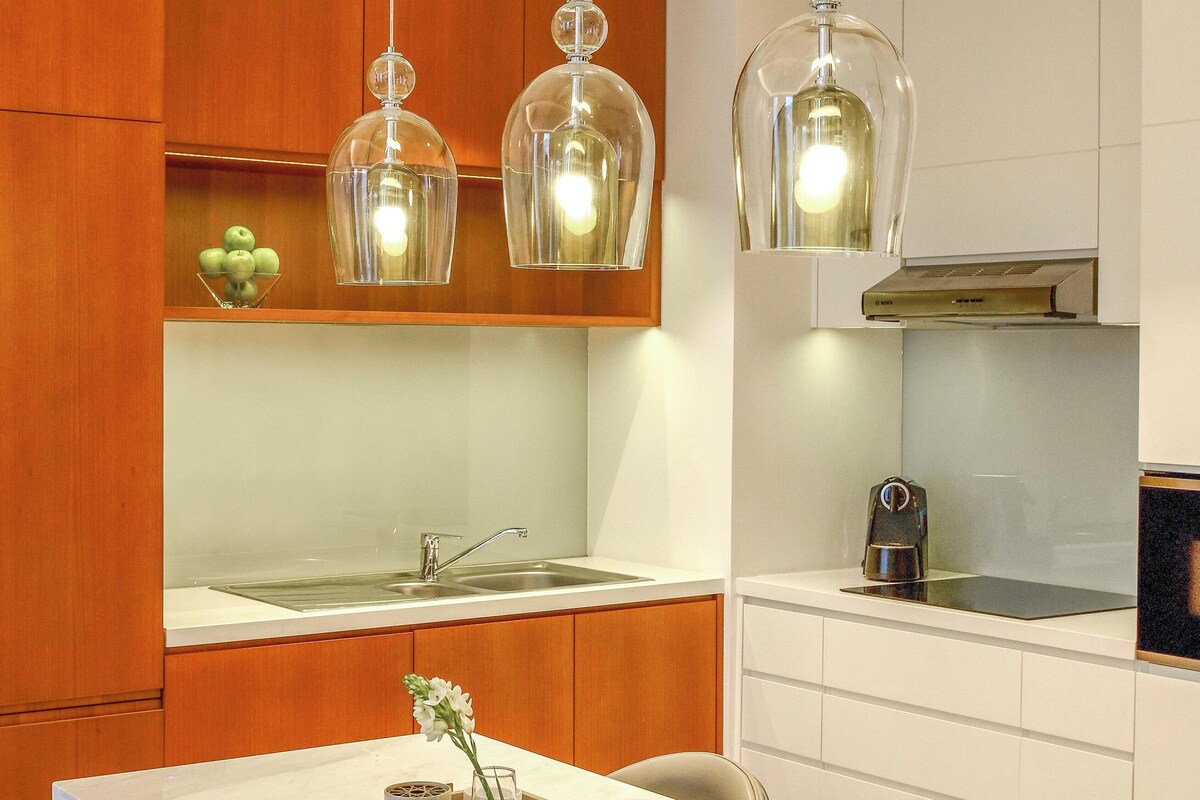 Une cuisine moderne avec des armoires blanches, des éléments décoratifs en bois et des luminaires suspendus.