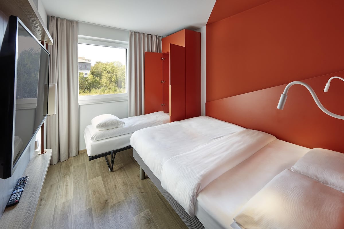 A hotel room with two beds, a TV, and a window with curtains.