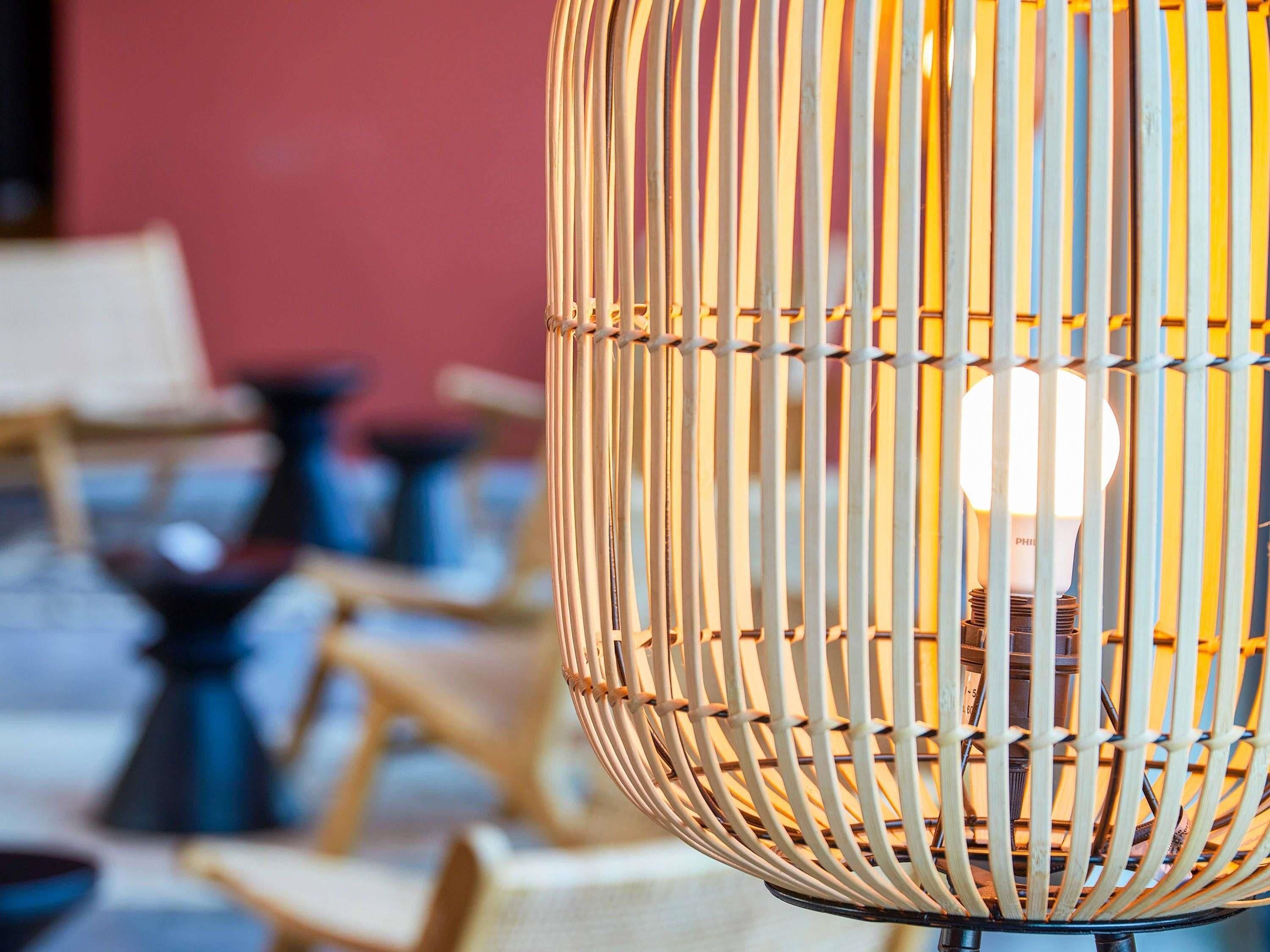 A wicker chair with a light bulb inside, set against a blurred background with a red wall.