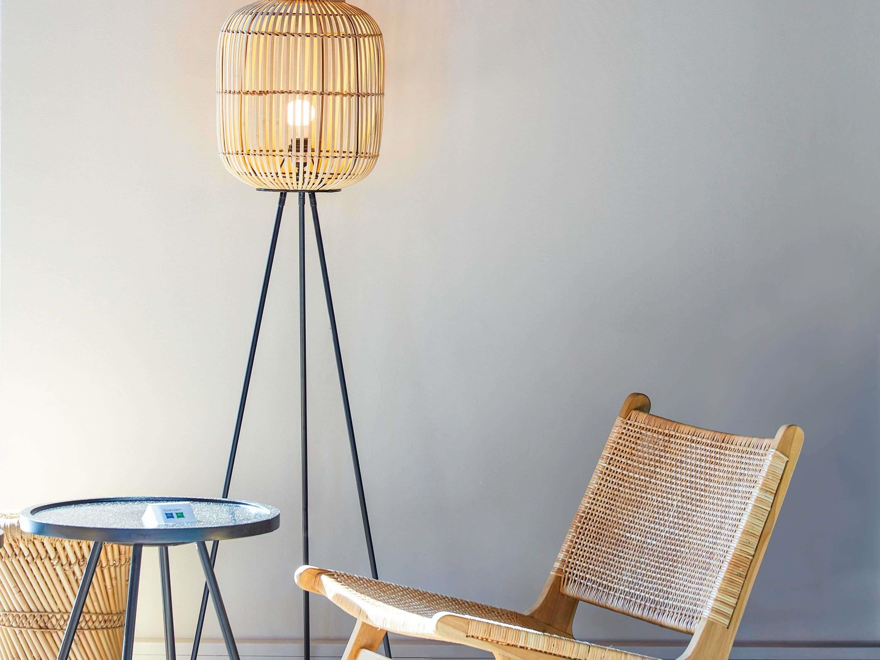 Una silla de mimbre y una pequeña mesa redonda en una habitación con una lámpara de pie alta.