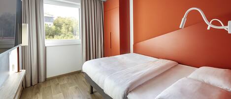 Habitación de hotel moderna con cama, televisor, ventana con cortinas y vista a zonas verdes.
