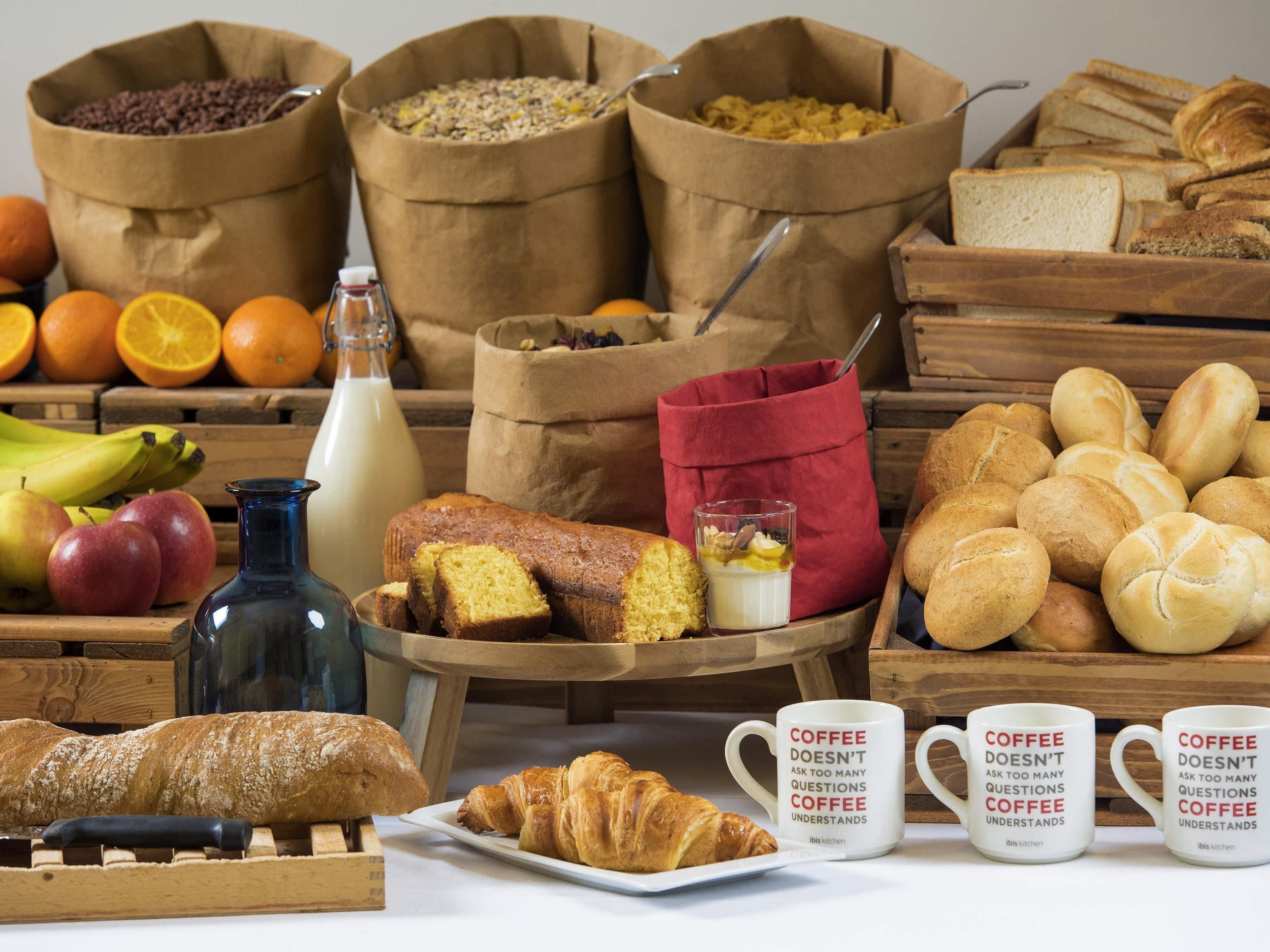 Desayuno con pan, bollería, frutas y tazas de café.