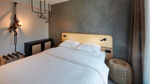 Una habitación de hotel moderna con una cama grande, una lámpara fijada a la pared y un pequeño reposapiés.